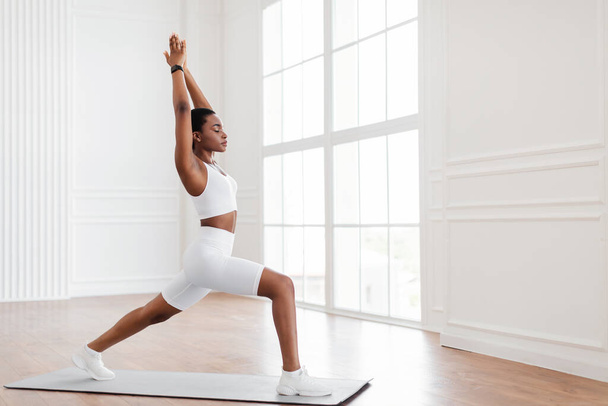 Young black woman doing warrior 1 pose on mat at home - Photo, Image