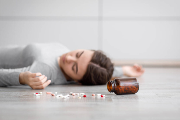 Sad european millennial lady unconscious lying on floor with scattered pills, committed suicide at home - Foto, Imagem