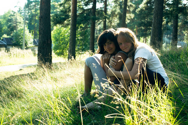 公園の緑の草の上に座っている二人の十代の女の子の友人. - 写真・画像