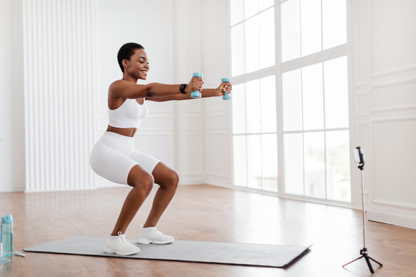 Young black woman exercising with dumbbells in front of smartphone - Foto, Imagem