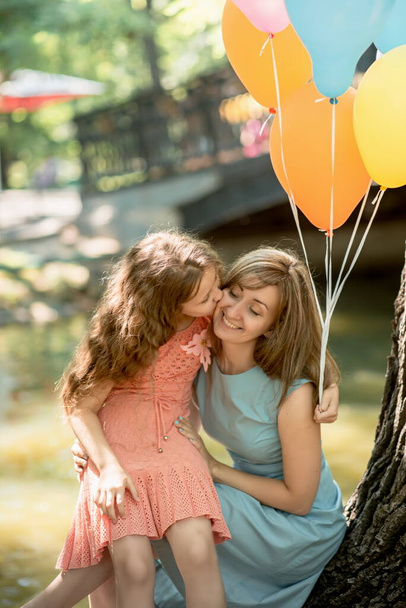Cute family mom and her daughter are launching balloons for birthday celebration in summer park - Photo, image