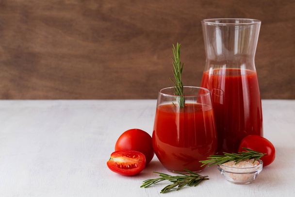 tomato juice and fresh tomatoes on the white background. glass of tomato juice with rosemary and salt on the table with copy space - Photo, Image