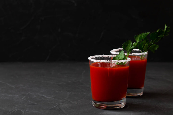 Kaksi lasillista tomaattimehua pippurilla, mausteilla, suolalla ja jäällä lasissa kopiointitilalla. Bloody Maryn cocktail. Alkoholijuoma vodkalla, vampiro cocktail mustalla taustalla. - Valokuva, kuva