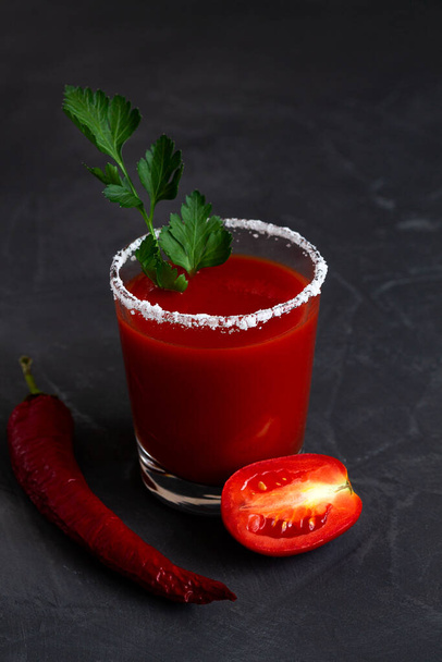 tomato juice in a glass.Tomato juice with pepper, spices, salt and ice in glass with copy space. Bloody Mary cocktail. Alcoholic drink with vodka, vampiro cocktail on the black background. vertical. - Photo, Image