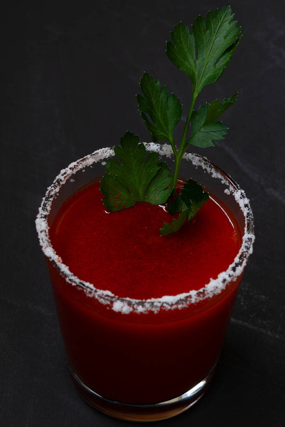 Close-up Tomatensap met selderij, specerijen, zout en ijs in glas met kopieerruimte. Bloody Mary cocktail. Alcoholische drank met wodka, vampiercocktail op de zwarte achtergrond. verticaal. - Foto, afbeelding