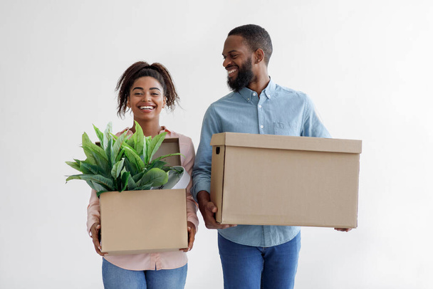 Щасливий молодий чорний чоловік і дружина тримають картонні коробки з горщиками, на білому тлі стіни
 - Фото, зображення