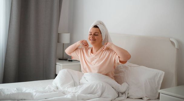 Young beautiful smiling girl stretching in her bed with white bedclothes. Concept of Good morning, enjoy new day, woman feels happy and peppy after enough sleeping - Fotó, kép