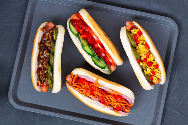 hot dog mustárral és ketchup.ízletes Hot dog különböző feltétekkel: uborka, sült hagyma, paradicsom és sárgarépa zöld, fekete háttér másolási hellyel. Lapos fekvés. Gyorsétterem-koncepció. - Fotó, kép