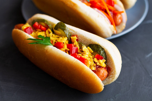 Nahaufnahme leckere hausgemachte Hot Dogs mit verschiedenen Belägen: Essiggurken, gebratene Zwiebeln, Tomaten und Karotten mit grünem Hintergrund auf schwarzem Hintergrund mit Kopierfläche. Fastfood-Konzept. - Foto, Bild