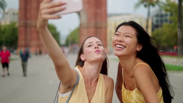 Kaksi onnellista sekarotuinen naisten ystäviä tehdä selfie ulkona ja valitsemalla paras kuva matkapuhelimella - Materiaali, video