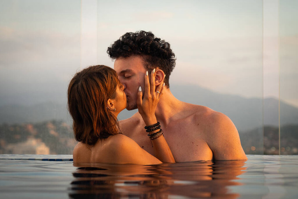 Amare coppia baciarsi nell'acqua palo infinito durante il tramonto. Concetto vacanza romantica  - Foto, immagini