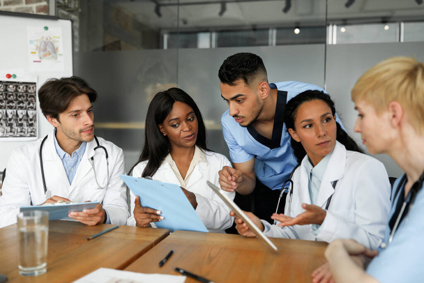 Equipe multiétnica concentrada de médicos sentados à mesa, conversando - Foto, Imagem