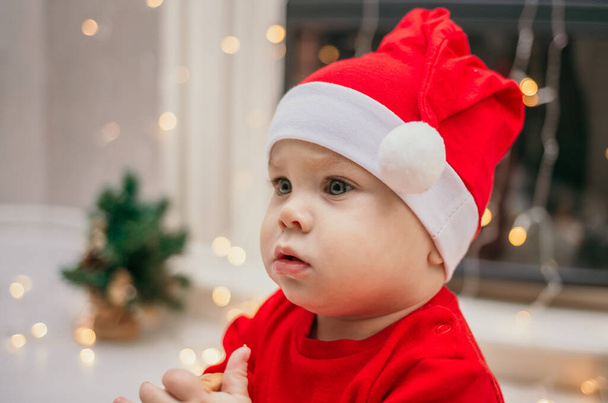 a little girl in a red Christmas hat is sitting in a room near the fireplace - Photo, Image