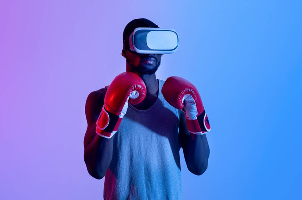 Jonge zwarte sportman in VR-headset en bokshandschoenen met virtuele training in neon licht - Foto, afbeelding