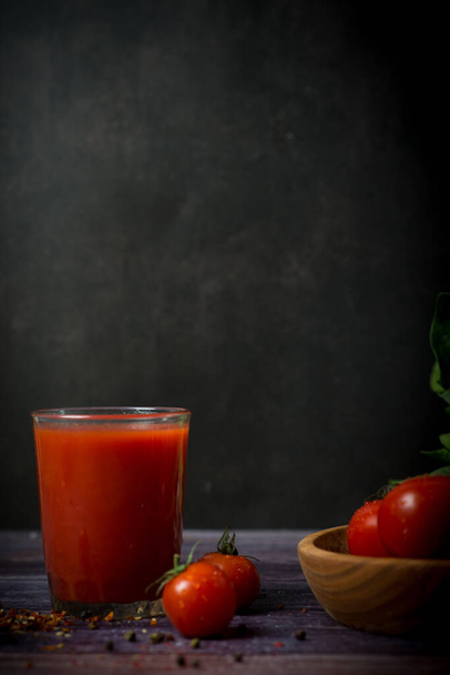 ντοματίνια και τοματοχυμό σε μαύρο φόντο. Κοκτέιλ ντομάτας με ντομάτες - Φωτογραφία, εικόνα