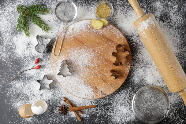 Festive kitchen flour background for making christmas gingerbread cookies with cutters, wooden rolling pin, fir branch,  winter spices and board on vintage table. Top view pastry card with copy space. - Foto, Imagem