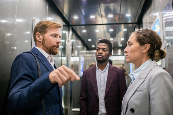 Zwei von drei interkulturellen Kollegen diskutieren im Fahrstuhl - Foto, Bild