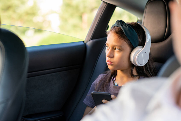 Cute poważna dziewczyna ze słuchawkami przewijanie w smartfonie - Zdjęcie, obraz