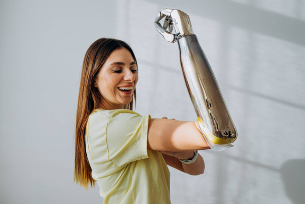 Portret van een sterke en onafhankelijke vrouw met een bionische prothetische arm toont een biceps op een lichte achtergrond - Foto, afbeelding