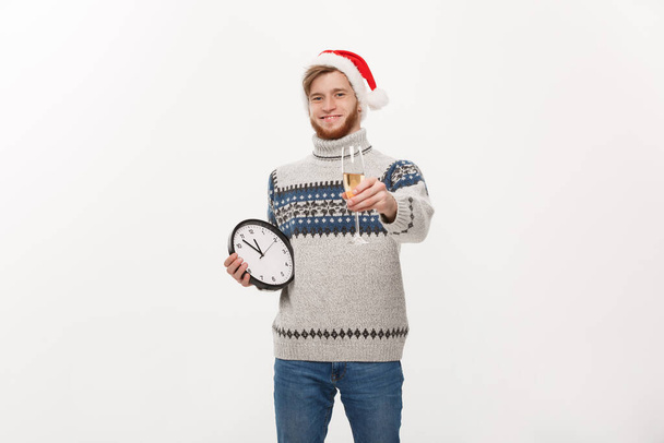 Koncepcja Holiday - młody przystojny broda człowiek w sweter z zegarem biały i szampana na tle białego studia. - Zdjęcie, obraz