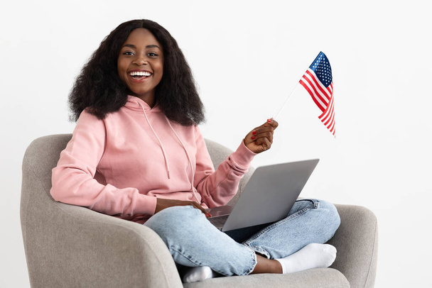 Dizüstü bilgisayarı olan siyah bir kadın ve koltukta Amerikan bayrağı. - Fotoğraf, Görsel