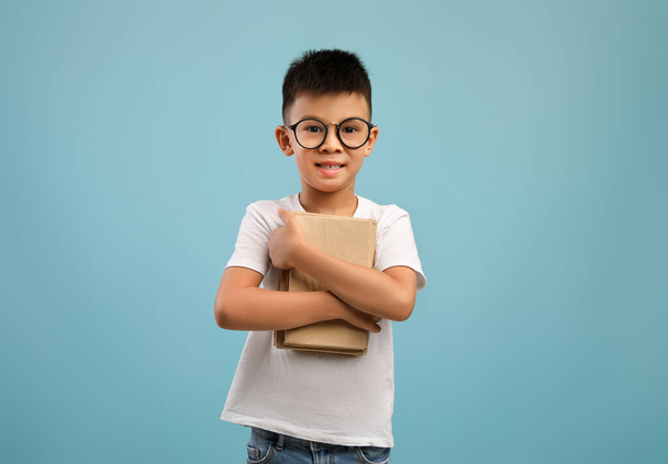 Cute little asian boy wearing eyeglasses holding stack of books - Foto, Imagen