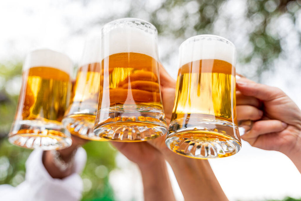 Group of people enjoying and toasting a beer outdoors - Close-up on four pint of beer - Friendship concept with young people having fun together - 写真・画像