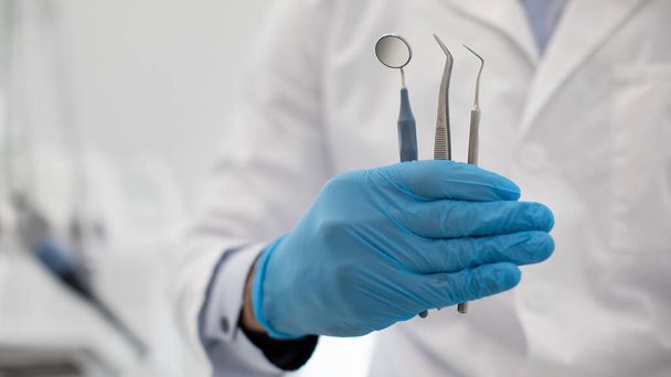 Μη αναγνωρίσιμος γιατρός οδοντίατρος σε μπλε αποστειρωμένο γάντι κρατώντας οδοντιατρικά εργαλεία στο χέρι - Φωτογραφία, εικόνα