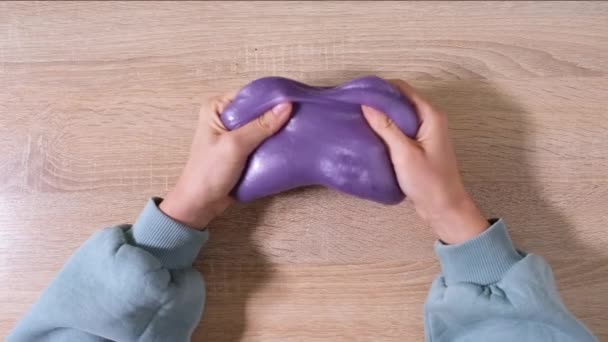 Spiel mit Schleim, Stretching der gooey Substanz für Spaß und Stressabbau. Nahaufnahme und Draufsicht der weiblichen Hand, die lila glänzenden Schleim hält und ihn zusammendrückt. 4K-Video. - Filmmaterial, Video