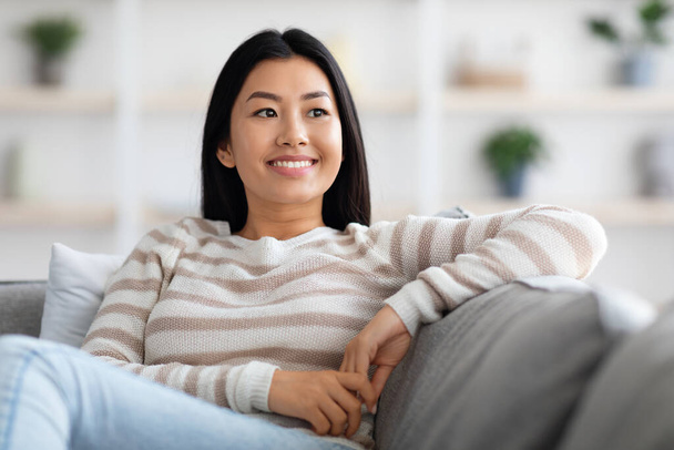 Portrait Of Beautiful Smiling Korean Woman Relaxing On Comfortable Couch At Home - Foto, afbeelding