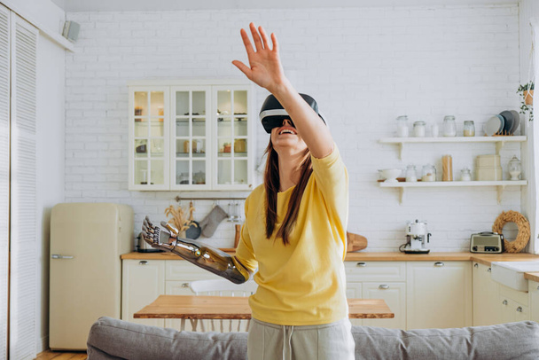 Женщина с бионической рукой и VR гарнитурой танцует на кухне - Фото, изображение
