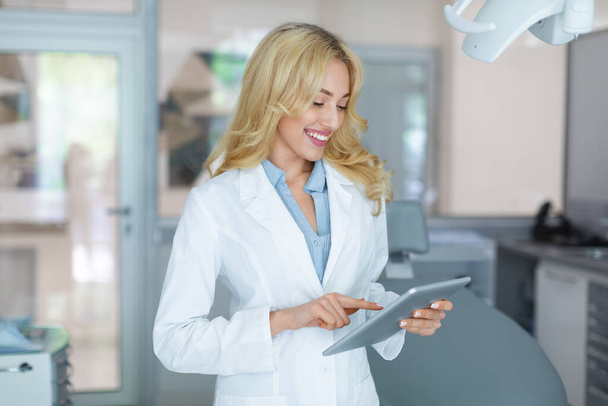 Attraente dentista femminile con tablet digitale sorridente mentre lavora - Foto, immagini