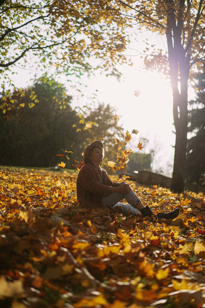 Young beautiful woman in a hat in an autumn park, a string bag with oranges, a woman throws up autumn leaves. Autumn mood, bright colors of nature. - Fotoğraf, Görsel