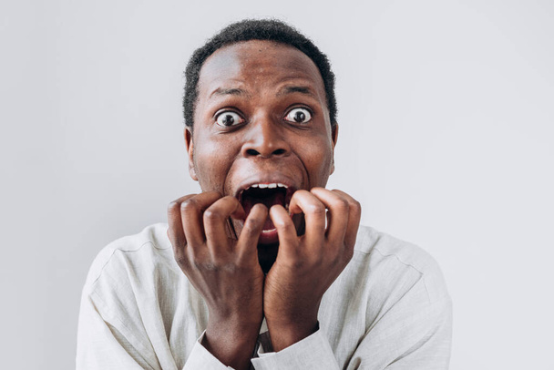Το πορτρέτο ενός τρομοκρατημένου Αφρικανού κοιτάζει με τρόμο την κάμερα και βάζει τα χέρια του στο στόμα του. - Φωτογραφία, εικόνα
