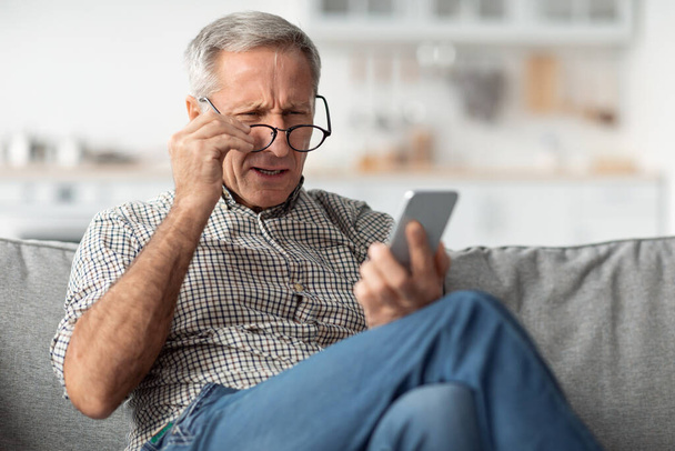 Hombre mayor entrecerrando los ojos Lectura Mensaje Usando anteojos en casa - Foto, Imagen