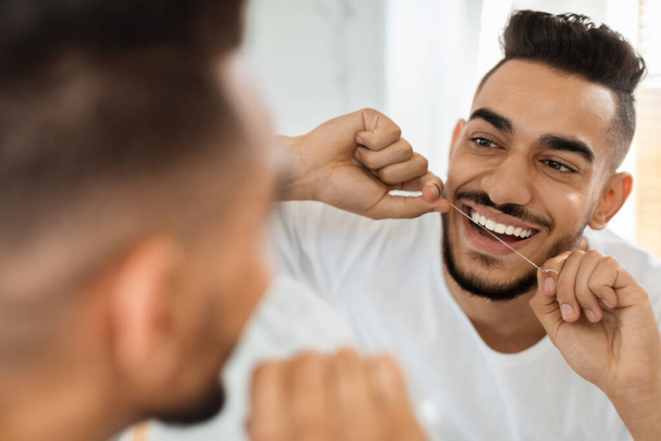 Oral Hygiene. Handsome Arab Guy Using Dental Floss While Looking In Mirror - Фото, зображення