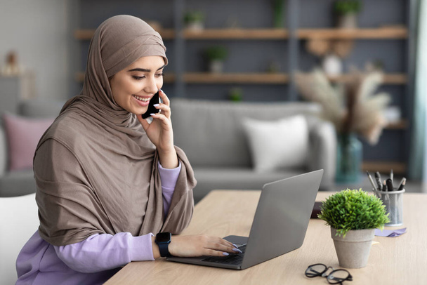 Femme musulmane souriante qui travaille et parle sur son téléphone portable à la maison - Photo, image