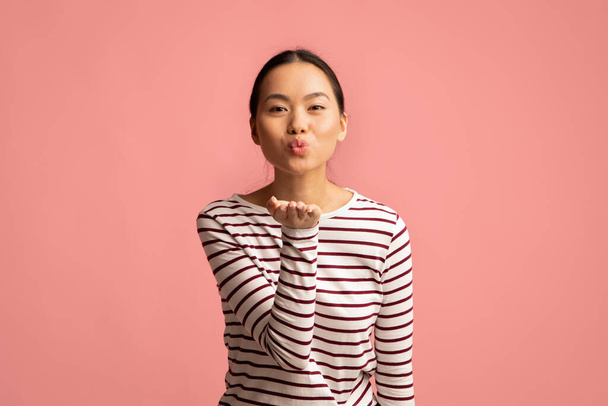 Giovane allegra asiatico donna broncio labbra e soffiaggio aria bacio a macchina fotografica - Foto, immagini