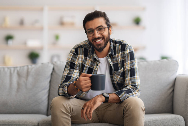 Handsome millennial arab man resting at home, drinking coffee - 写真・画像