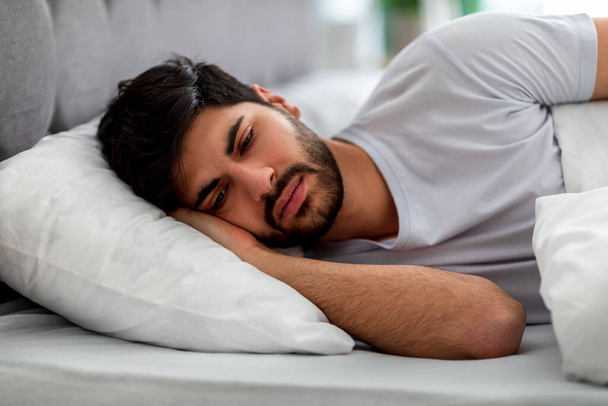 Sad arab guy lying alone in bed, suffering from loneliness and thinking of problems. Male stress and depression concept - Photo, Image