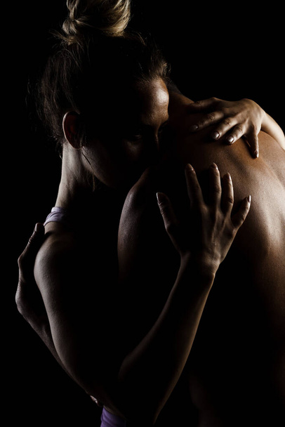 Fit couple posing together. Boy and girl side lit silhouettes on black background. - 写真・画像