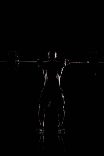 Athlete lifting barbell. Silhouette of a muscular man. - Photo, image