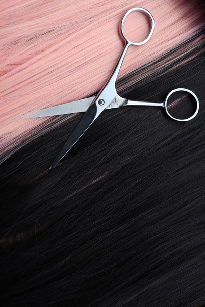 Tijeras de corte de cabello sobre fondo de pelo negro y rosa - Foto, Imagen