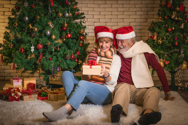 caucasian senior couple feel happy giving present and celebrate Christmas night together with decorated Christmas tree at home - 写真・画像