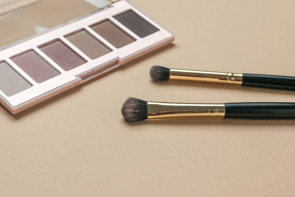 Two brushes and a set of eye shadow on a beige background. Stylish women's cosmetics. - Photo, Image