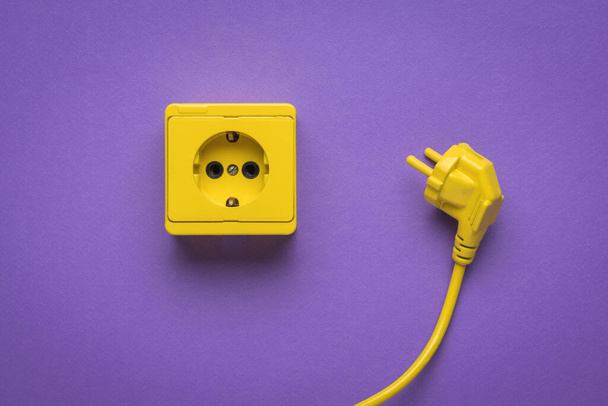 Желтый шнур питания и желтая розетка на ярком фиолетовом фоне. Стильный дизайн. Место, где подключены электроприборы. - Фото, изображение
