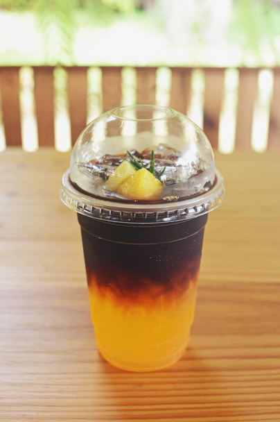 Візьміть пластикову чашку замороженої чорної кави (американо) на дерев "яному столі в саду. - Фото, зображення