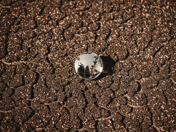 Glass globe on brown dried crack soil land background, top view. Crystal earth on crack floor background. Dryland. Global warming. Global heat effect. - Photo, Image