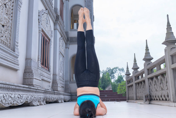 Mujer asiática joven está haciendo ejercicio con ejercicios de yoga difíciles en la mañana frente al patio del templo para tener buena salud para comenzar una jornada laboral efectiva. - Foto, imagen