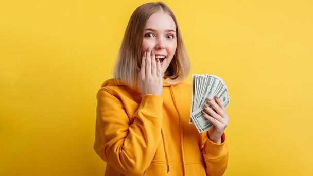 Happy excited rich young woman win money cash. Lady hold Dollar stack surprised rejoices at lottery victory isolated over yellow color background. Long web banner - Foto, Imagen